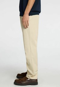 Beige bomullsbukser med rak passform, sidfickor och en mjuk textur, parat med mörkbruna skor med dekorativa tofsar.