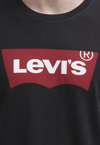 Svart T-shirt med en röd Levi's-logotyp som innehåller vit fet text och ett registrerat varumärke-symbol på bröstet.