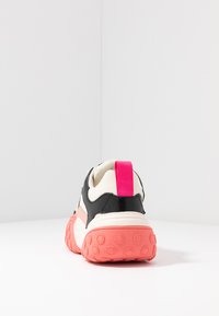 Schwarz-weißer Sneaker mit einer rosa- und korallenfarbenen Sohle, der an der Ferse einen rosa Zuglasche und eine strukturierte Gummisohle für besseren Grip hat.