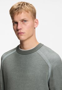 Γκρι ριγέ πουλόβερ με στρογγυλεμένο λαιμό, που διαθέτει ανοιχτό γκρι λεπτομέρειες στους ώμους και υφασμάτινη υφή. Λεπτό φινίρισμα, καθημερινός σχεδιασμός.