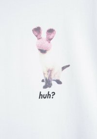 Kot syjamski w różowej, dzierganej masce z uszami królika, siedzący na białym tle z napisem „co?” poniżej.