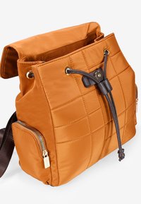 Borsa in nylon arancione trapuntata con chiusura a coulisse, dettagli marroni e tasche laterali con zip. Presenta una texture morbida e una forma rettangolare.