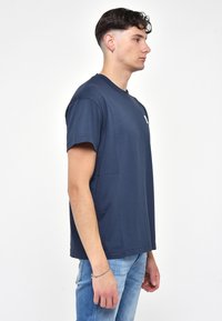 Námořnická modrá bavlněná trička s krátkým rukávem, kulatým výstřihem a malým logem na hrudi. Jednoduchý, uvolněný střih.
