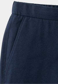 Pantalon bleu marine en gros plan montrant une ceinture élastique et une poche latérale diagonale avec des détails de couture visibles.