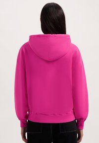Roze hoodie met een ruime pasvorm, ribgebreide manchetten en onderkant. Zachte textuur, afgewerkte naden en een ruime capuchon.