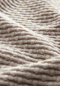 Tissu tricoté en marron clair avec des textures côtelées et lisses alternées, présentant un motif ondulé sur toute la surface. Matière douce et souple.