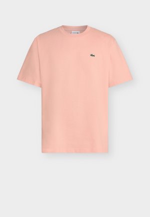 T-shirt rose clair à manches courtes avec col rond et petit logo crocodile vert sur la poitrine gauche.