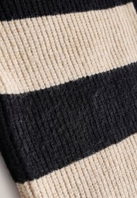 Ribbet stof med skiftevis sorte og cremefarvede striber; teksturen er blød med en let fluffy overflade.