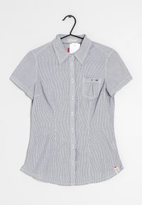 Košile s krátkým rukávem na knoflíky v modrých a bílých pruzích. Má špičatý límec, náprsní kapsu a bílé knoflíky s mírně zaobleným spodním okrajem.