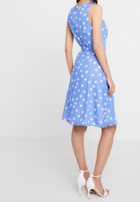 Robe sans manches bleu clair avec des pois blancs, taille cintrée, jupe évasée, finie avec une texture lisse et un éclat subtil.