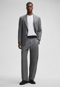 Szary, fakturowany żakiet w stylu marynarki z dwoma guzikami, zestawiony z luźnymi szarymi spodniami. Nosi się go na białej koszuli, dopełniony czarnymi butami.