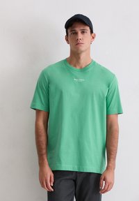 Zielony, bawełniany T-shirt z krótkim rękawem, z okrągłym dekoltem i białym logo nadrukowanym na piersi. Gładka faktura, luźny krój.