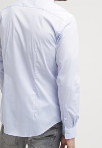 Camicia azzurro chiaro a maniche lunghe con colletto standard, polsini con bottone e una texture liscia con una spalla posteriore.
