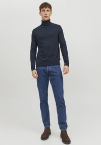 Pulover din tricot cu guler înalt de culoare bleumarin, asortat cu blugi de denim albaștri. Ținuta este completată cu botine maro.