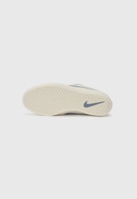 Nike sportbačių padas, pasižymintis tekstūruota kreminės spalvos gumine danga su raštuota padu ir pilku Nike logotipu. Sklandus siluetas ir ergonomiška forma.