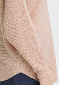 Pull en maille rose clair avec un design texturé côtelé et une coupe légèrement courte, doté d'un ourlet festonné et de manches longues.