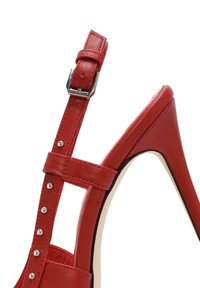 Sandal con tacco alto in pelle rossa, dotata di cinturino alla caviglia con fibbia argentata, dettagli borchiati e tacco affusolato per un design elegante.
