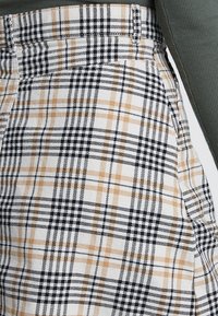 Pantalones de cuadros en blanco, negro y marrón; presentan un patrón de cuadros con anchos variables. La tela tiene una textura suave.