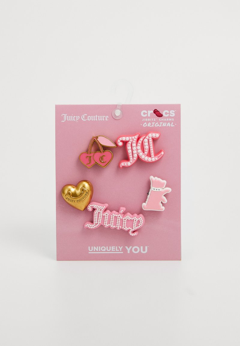 Viisi Crocs Jibbitz -korua: kultainen sydän, vaaleanpunainen "Juicy" -logo, vaaleanpunainen "JC" -logo, punaiset kirsikat ja vaaleanpunainen eläinhahmo vaaleanpunaisella taustalla.