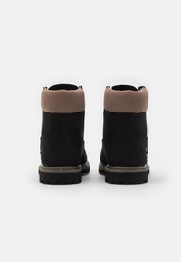 Bottes en daim noir avec un col en tricot marron, une semelle en caoutchouc et des surpiqûres décoratives. Présentent un design texturé et un col rembourré pour plus de confort.