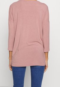 Maglione oversize a maniche lunghe in rosa polveroso, con un ampio scollo a barca e un tessuto morbido. Design senza cuciture con orlo arrotondato.