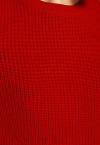 Roter gerippter Pullover mit Rundhalsausschnitt und strukturiertem Material. Der Stoff zeigt ein einheitliches Muster auf der gesamten Fläche.