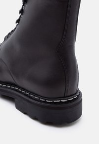 Κοντινή λήψη της φτέρνας μαύρου δερμάτινου αρβυλού μάχης με παχιά μαύρη σόλα και λευκή ραφή σε λευκό φόντο.