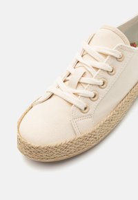 Zapatilla de lona en color blanco roto con ojales beige y cierre de cordones. Cuenta con una planta media de yute tejido y textura suave. Diseño de puntera redonda.