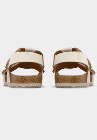 Μπεζ σανδάλια με ανοιχτή πλάτη, διαθέτουν δύο φαρδιές λουρίδες και πάτους από φελλό, εμφανιζόμενα από πίσω σε λευκό φόντο.