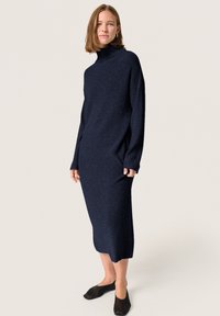 Rochie tricotată bleumarin, cu guler înalt, mâneci lungi și o siluetă dreaptă, asortată cu pantofi slip-on negri.