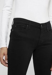 Svarta denimjeans med medelhög midja, framfickor och en mjuk textur. Matchas med en vit långärmad topp.