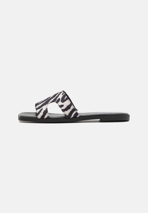 Sort flad slidesandal med bred zebra-print rem med udskæringsdetalje på hvid baggrund.
