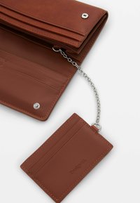 Brown leather wallet with a textured finish, featuring a zippered compartment, card slots, and a detachable chain holding a cardholder.