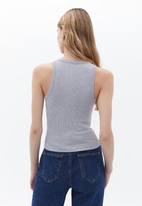 Šedý žebrovaný top na ramínka s těsným střihem, širokým výstřihem a bez rukávů, spárovaný s tmavě modrými džíny s vysokým pasem.