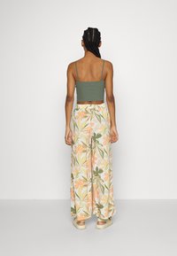 Débardeur court vert olive associé à un pantalon large orné d'un motif floral en pêche, jaune et vert. Coupe décontractée, tissu léger.