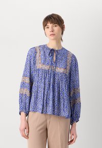 Blå trykt bluse med rund hals, bindedetalj og luftige ermer. Har geometriske og blomster mønstre i oransje og hvitt.
