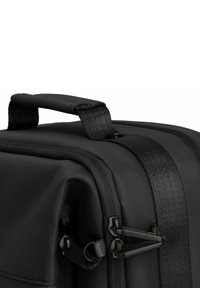 Zwarte stoffen tas met een gestructureerd oppervlak, voorzien van een stevige handgreep en contrasterende zwarte ritssluitingen. Compacte en rechthoekige vorm.