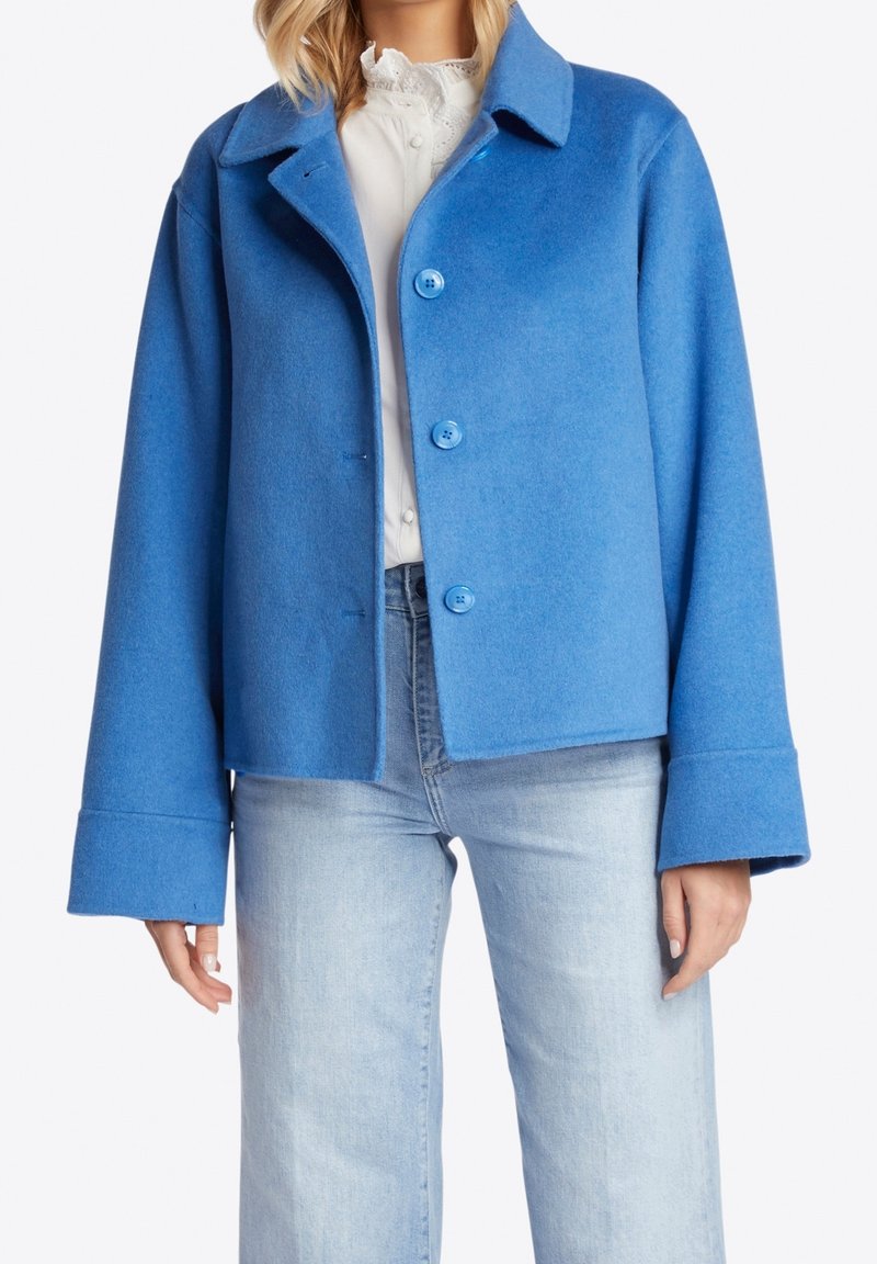 Blå uldblandet jakke med krave og fire store knapper, med brede ærmer og cropped design. Kombineret med lyse denimjeans.