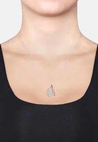 Silberne Halskette mit einem runden Anhänger mit geometrischem Muster und einem Akzent in Roségold in Form einer Feder, getragen auf einem schwarzen Oberteil.