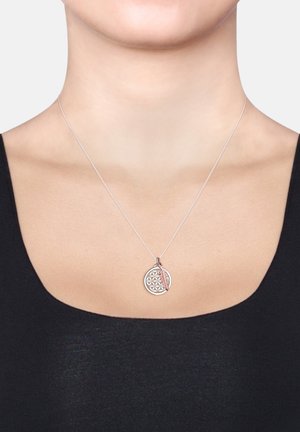 Silberne Halskette mit einem runden Anhänger mit geometrischem Muster und einem Akzent in Roségold in Form einer Feder, getragen auf einem schwarzen Oberteil.