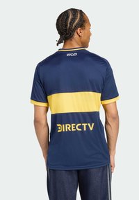 Tamsiai mėlynas sportinis marškinėlis su geltonu juostele viduryje ir didelėmis geltonomis raidėmis ant nugaros, kuriose užrašyta "DIRECTV". Trumpomis rankovėmis.
