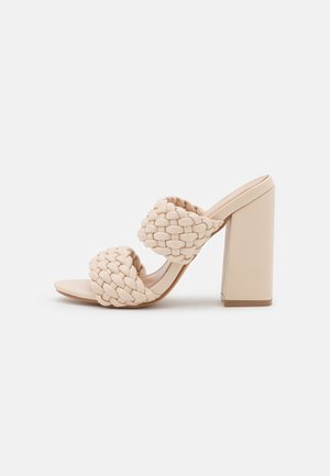 Beige højhælede sandal med to tykke vævede remme og en bred blokhæm på en hvid baggrund.