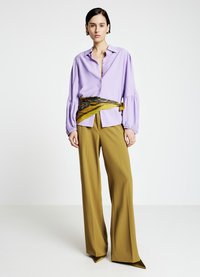 Chemise lavande boutonnée avec manches ballon, associée à un pantalon taille haute moutarde. Accentué par une ceinture jaune et verte à motifs.