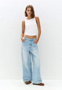 Top corto bianco abbinato a jeans a gamba larga blu chiaro. I jeans presentano un lavaggio sbiadito e sono accentuati da tasche standard.