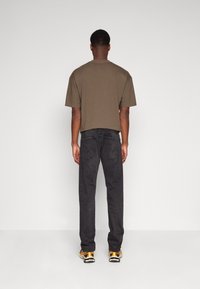 Camiseta de manga corta verde oliva, jeans de mezclilla negros y zapatillas multicolores vistas desde atrás sobre un fondo neutro.