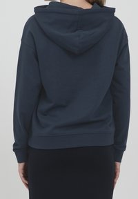 Marinblå bomullshoodie med design på baksidan, dragsko på huvan samt ribbade ärmslut och nederkant. Slät textur, avslappnad passform.