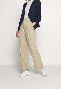 Navy blazer over a white t-shirt, with beige striped wide-leg trousers and white sneakers. The fabric appears smooth with structured design.