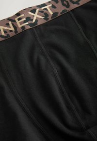 Juoda audinio boxer tipo apatiniai turi lygų tekstūrą, leopardų rašto juostos ir auksinį užrašą "NEXT".