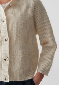 Cremfarbener Cardigan aus weichem Strickstoff mit strukturiertem Streifenmuster, verfügt über große Knöpfe und einen lässigen Schnitt.