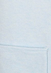 Helles blaues Strickgewebe mit einer glatten Textur und einem Taschen Detail am Boden. Der Stoff wirkt weich und leicht dehnbar.